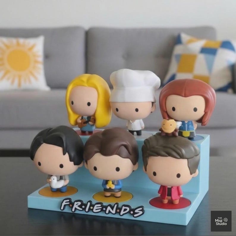 May include: A set of six Friends character figurines displayed on a light blue stand. Each figure has a unique hairstyle and outfit, with the word "FRIENDS" printed on the stand. The figurines are in a cartoon style.