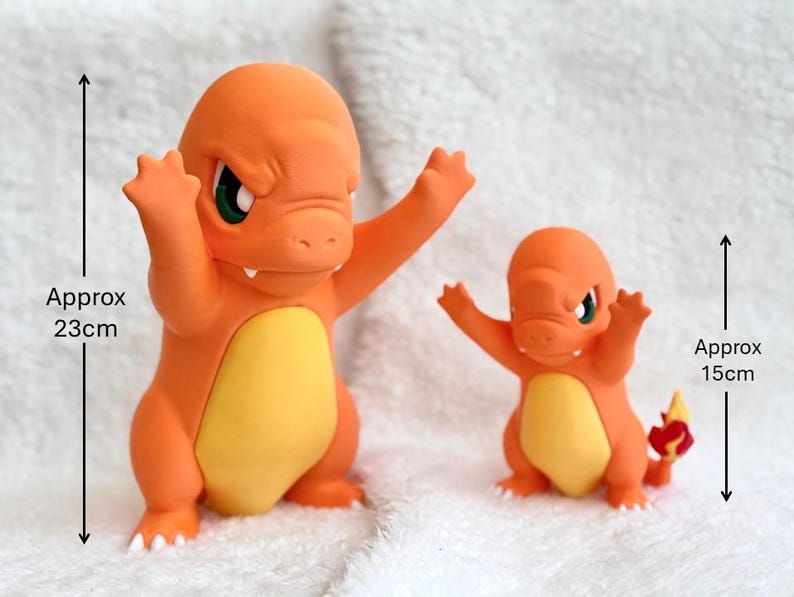May include: Two orange and yellow Charmander figures with green eyes and raised arms. The larger figure measures approximately 9.06 inches in height, while the smaller figure measures approximately 5.91 inches in height, as indicated by the text.