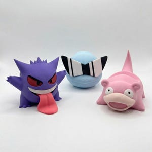 May include: Three small character figurines: a purple creature with red eyes and a long pink tongue, a light blue round creature wearing large black and white sunglasses, and a pink creature with a wide mouth and a pointed tail on its back.