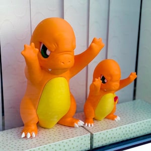 Puede incluir: Dos figuras de lagarto b&iacute;pedo de color naranja y amarillo con cabezas grandes, ojos verdes y garras blancas. Las figuras est&aacute;n posadas con los brazos levantados en una postura din&aacute;mica, con superficies mate lisas y parches amarillos.