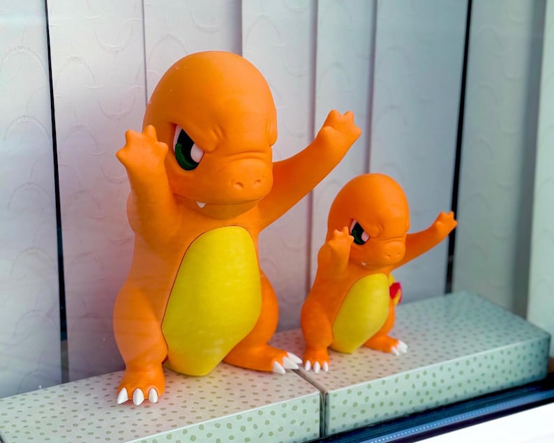 Puede incluir: Dos figuras de lagarto b&iacute;pedo de color naranja y amarillo con cabezas grandes, ojos verdes y garras blancas. Las figuras est&aacute;n posadas con los brazos levantados en una postura din&aacute;mica, con superficies mate lisas y parches amarillos.