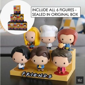 May include: A set of six Friends character figurines displayed on a yellow stand with the show's logo. The figurines have large heads and are in various outfits. The text "INCLUDE ALL 6 FIGURES - SEALED IN ORIGINAL BOX" is visible.