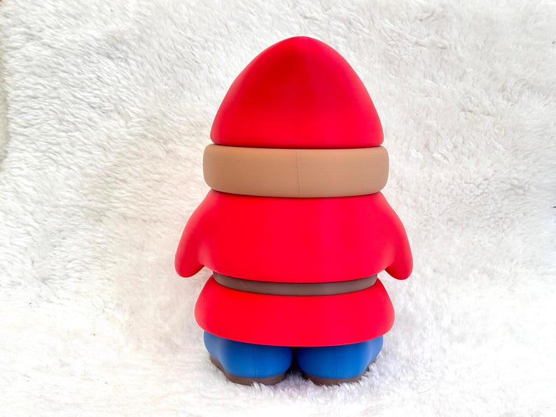 May include: A gnome figurine featuring a bright red pointed hat, a tan band around the hat, a red tunic with a brown belt, and blue boots. The figure has a smooth, matte finish and is shown from the back, displaying a solid, uniform color scheme.