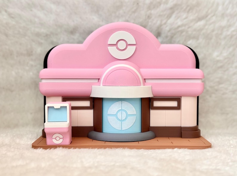 May include: A pink and white 3D-printed model of a building with a stylized design. The building features a central entrance with a blue and white design, a pink roof with a white emblem, and a small pink kiosk.