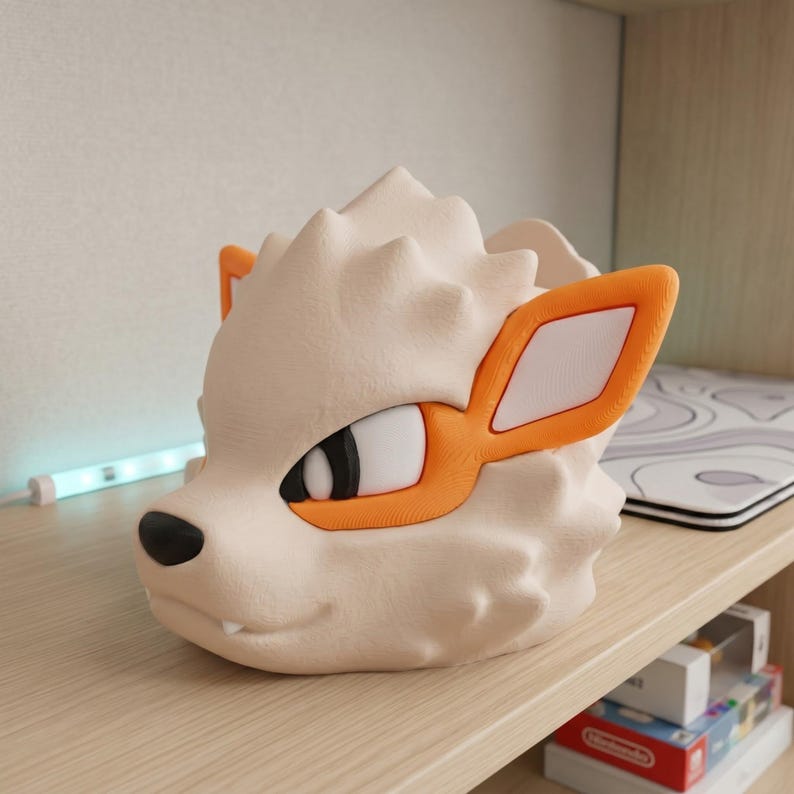 May include: A cream-colored, 3D-printed sculpture of a stylized canine head with orange accents around the eyes and ears. The sculpture has a textured surface and a black nose. The design is reminiscent of a popular animated character.