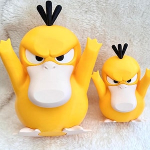 Puede incluir: Dos figuras amarillas parecidas a patos con mechones de pelo negros, picos blancos y pies blancos. La figura m&aacute;s grande mide aproximadamente 23 cm de altura, mientras que la m&aacute;s peque&ntilde;a mide 15 cm. Ambas figuras tienen expresiones de enojo.