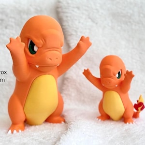 Puede incluir: Dos figuras de Charmander de color naranja y amarillo con ojos verdes y brazos levantados. La figura m&aacute;s grande mide aproximadamente 23 cm de altura, mientras que la m&aacute;s peque&ntilde;a mide aproximadamente 15 cm, seg&uacute;n indica el texto.