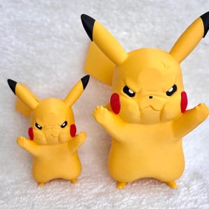 May include: Two yellow Pikachu figures with black-tipped ears and red circular cheeks. Both figures feature a stern, frowning facial expression with furrowed brows, standing with arms raised in a defensive posture, rendered in a smooth matte finish.