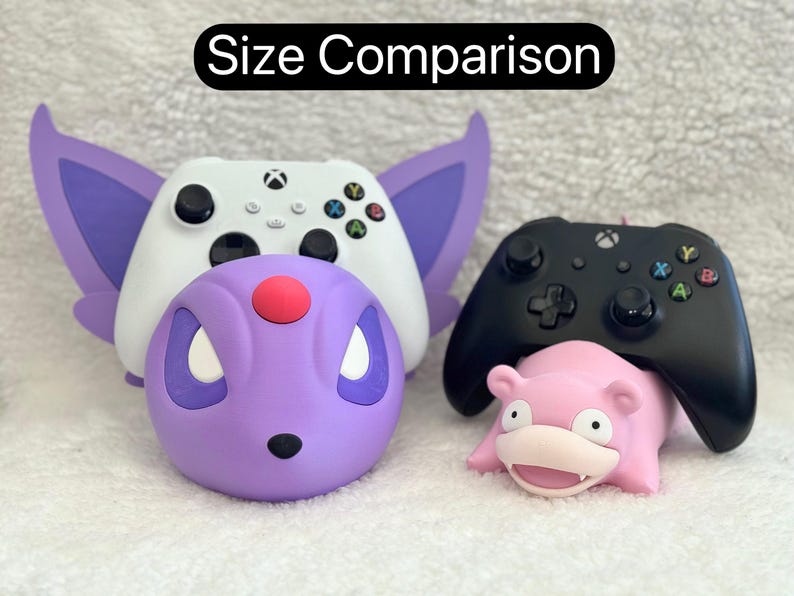 Puede incluir: Un mando de Xbox blanco sobre un soporte morado con forma de criatura y orejas grandes, junto a un mando de Xbox negro sobre un soporte rosa con forma de criatura. El texto "Size Comparison" aparece en la parte superior.