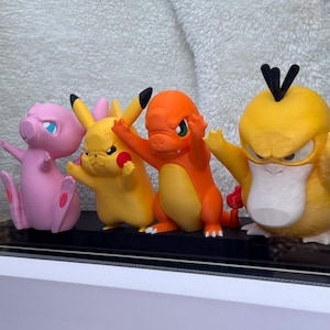 Puede incluir: Cuatro figuras de personajes de pl&aacute;stico de colores alineadas. De izquierda a derecha, una criatura rosa claro, una criatura amarilla con orejas puntiagudas, una criatura naranja con cola de llama y una criatura amarilla con pico plano y pelo negro.