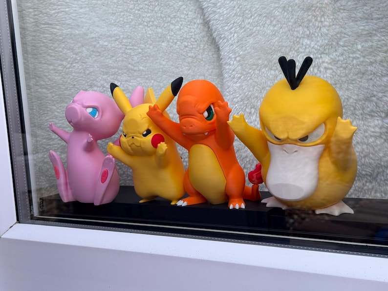 Puede incluir: Cuatro figuras de personajes de pl&aacute;stico de colores alineadas. De izquierda a derecha, una criatura rosa claro, una criatura amarilla con orejas puntiagudas, una criatura naranja con cola de llama y una criatura amarilla con pico plano y pelo negro.