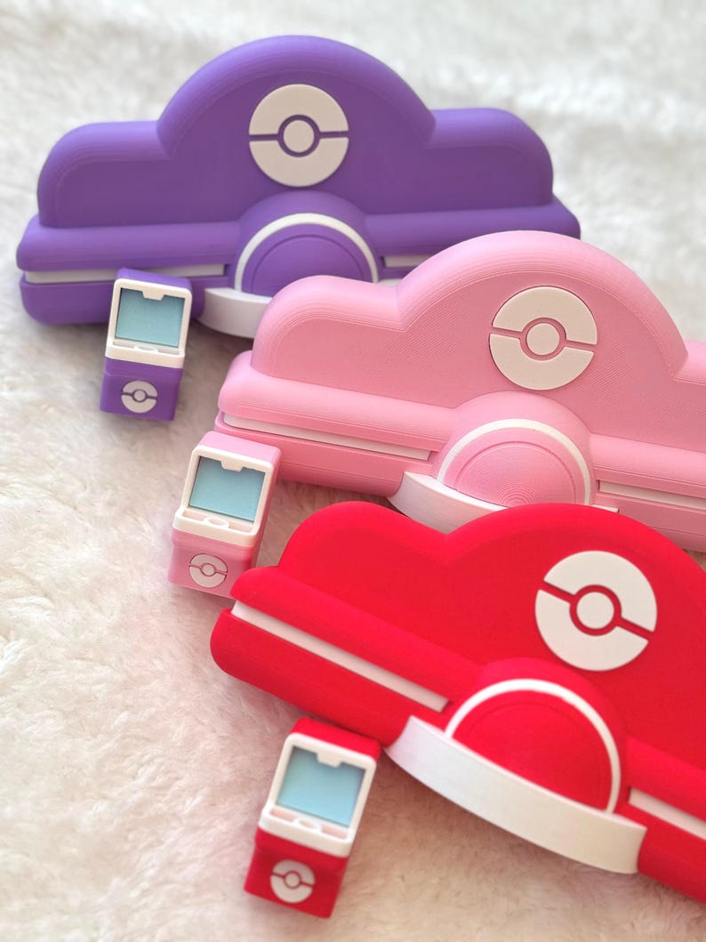 May include: Three colorful, stylized cloud-shaped accessories in purple, pink, and red, each with a white circular emblem. Accompanying each cloud is a matching small, rectangular device with a light blue screen and a similar emblem.