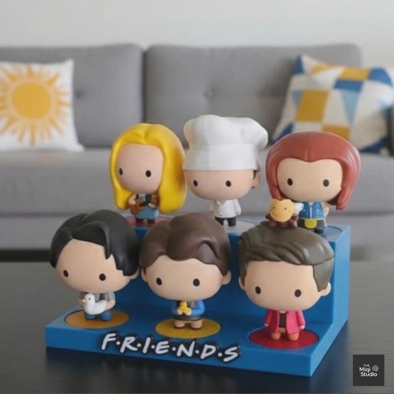 May include: A set of seven cartoon figurines of characters from the TV show "Friends". The figurines have large heads and small bodies, with distinctive hairstyles and outfits. They are displayed on a blue base with the show's logo.