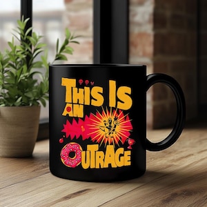 以下が含まれることがあります： 「THIS IS AN OUTRAGE」の文字が黄色とオレンジ色で描かれた黒いセラミックマグカップ。デザインには漫画の爆発、ドーナツ、トロフィーが含まれています。マグカップは黒いハンドルで、木製の表面に置かれています。