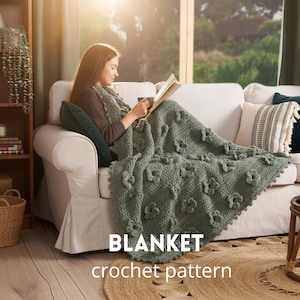 Puede incluir: Una manta de ganchillo verde salvia con detalles de flores, sobre un sofá blanco. La manta es el punto focal, con las palabras "BLANKET" y "crochet pattern" en texto blanco en la parte inferior. La escena está ambientada en un salón acogedor.