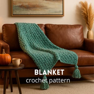 Puede incluir: Una manta de ganchillo turquesa con un patrón texturizado sobre un sofá de cuero marrón. La manta tiene dos borlas en los extremos. Una pequeña mesa de madera tiene una calabaza y una taza. El texto "BLANKET crochet pattern" está en la parte inferior.