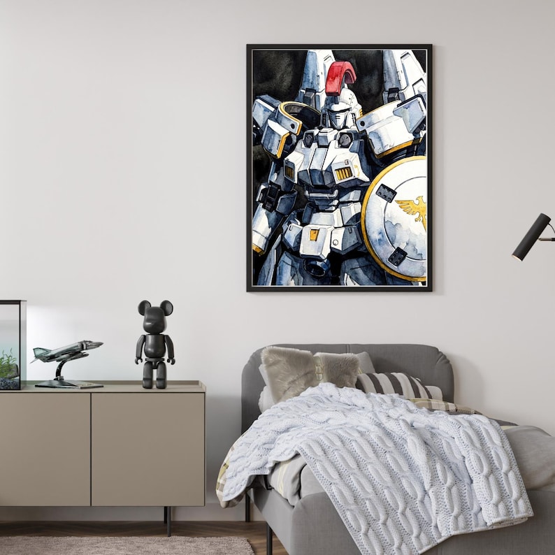 A black-framed watercolor portrait of the tallgeese gundam hanging in a modern bedroom above a gray bed with a knitted throw. This classic anime robot wall art showcases the iconic white mecha with its red crest and golden shield emblem, adding a clean sci fi touch to the room's decor.