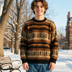 May include: A person wearing a patterned brown, black, and tan sweater with blue jeans and brown boots. The sweater has a repeating pattern of figures. The background includes a snowy path, trees, a bench, and a building.