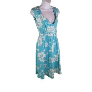 May include: A sleeveless, knee-length dress in a light blue hue, adorned with a white floral pattern. The dress features a cowl neckline and a fitted waist, creating a flattering silhouette. The fabric appears lightweight and suitable for warm weather.