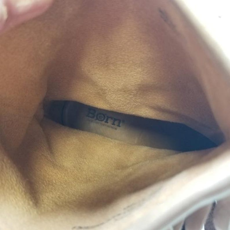 May include: Interior view of a light brown boot with the brand name "Born" visible on the insole. The boot's interior is a lighter shade of brown, with a soft, textured appearance. The boot's opening is visible at the top.