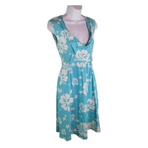 May include: A sleeveless, knee-length dress in a light blue hue, adorned with a white floral pattern. The dress features a cowl neckline and a fitted waist, creating a flattering silhouette. The fabric appears soft and flowing, suitable for warm weather.