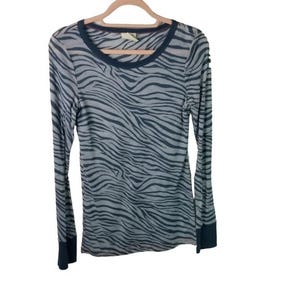 May include: A long-sleeved top featuring a grey and black zebra print. It has a dark blue crew neck and cuffs. The garment is displayed on a wooden hanger.