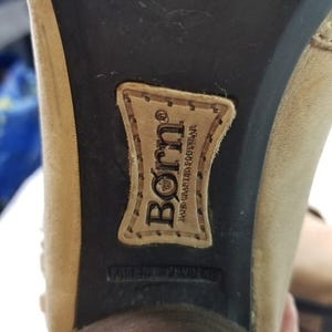 May include: Close-up of the sole of a beige-colored shoe. The brand name "Born" is visible on a stitched leather patch. The words "Hand Crafted Footwear" and "Patent Pending" are also visible.