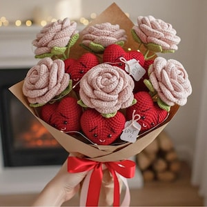 May include: A bouquet of handmade crochet flowers and hearts. The bouquet features pink roses and red hearts with smiling faces, wrapped in brown paper and tied with a red ribbon. Small tags with the words "Love is" are attached.