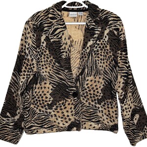 Könnte beinhalten: Ein langärmeliger Blazer mit einem gewebten Tiermuster in den Farben Schwarz, Dunkelbraun und Beige. Das Kleidungsstück verfügt über einen fallenden Reverskragen, einen einzelnen Knopfverschluss vorne und eine strukturierte Passform.