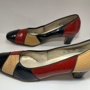 May include: A pair of vintage low-heeled shoes. The shoes feature a patchwork design with black, red, and tan sections. The heels are black, and the shoes have a glossy finish. The shoes are size 10.