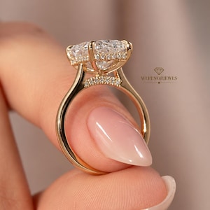 May include: A gold ring featuring a large, clear, faceted cushion-cut center stone set in a high-profile basket. The basket and bridge are accented with small pavé-set stones. The text WLPENORJEWELS is visible on the right side of the ring.