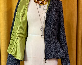 May include: A grey and black tweed jacket with a zip-up front and a peplum hem is displayed on a mannequin. The jacket has a bright green satin lining. A layered necklace and a long silver pendant are also on the mannequin.