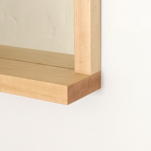 May include: Close-up of a light wood shelf with a square edge. The shelf is attached to a wall and is part of a larger wooden frame.
