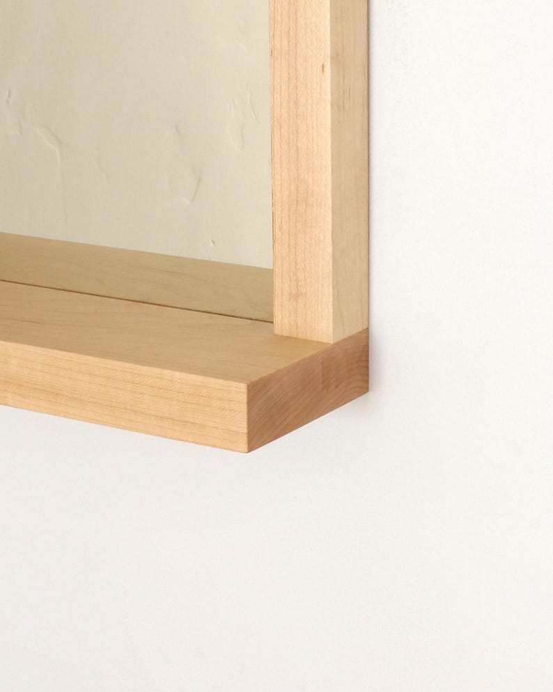 May include: Close-up of a light wood shelf with a square edge. The shelf is attached to a wall and is part of a larger wooden frame.
