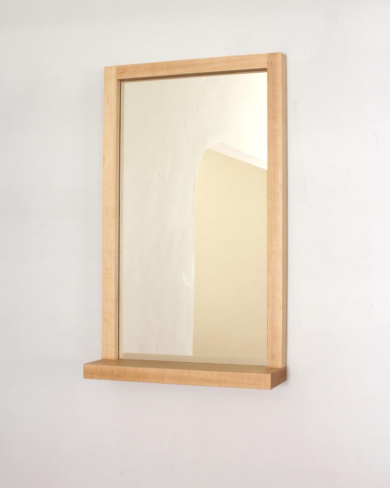 May include: A rectangular wooden mirror with a shelf underneath. The mirror has a light wood frame and the shelf is made of the same wood.