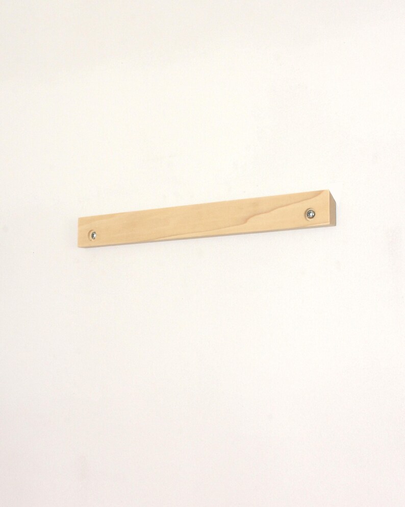 May include: A natural wood shelf with a light brown finish. The shelf is mounted to a white wall with two screws.