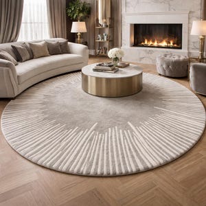 May include: A large circular area rug featuring a solid light gray center surrounded by a wide border of radiating white and gray linear patterns that extend outward toward the edge, creating a textured visual effect on the floor surface.
