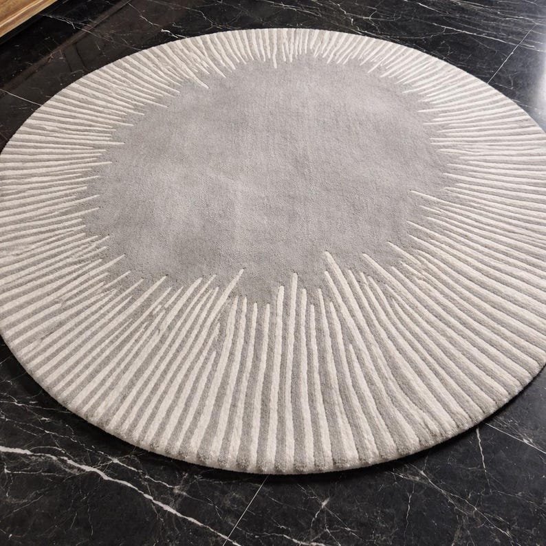 May include: A circular area rug featuring a solid light gray center surrounded by a wide border of radiating white lines. The design creates a sunburst pattern with varying lengths of white tufted lines extending outward from the central gray circle.