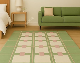 May include: A rectangular green rug with a geometric pattern. The rug features a grid design with alternating cream-colored squares and pink rectangles. Beige lines create the grid pattern. The rug is placed in a room with a green sofa and wooden furniture.