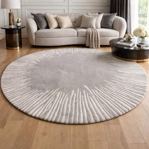 May include: A large, circular area rug featuring a solid light gray center surrounded by a textured border of radiating white lines that extend toward the outer edge, creating a sunburst-like pattern across the entire round floor covering.