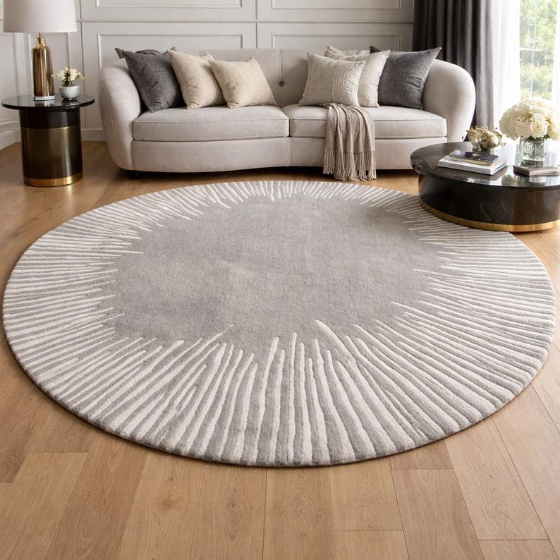 May include: A large, circular area rug featuring a solid light gray center surrounded by a textured border of radiating white lines that extend toward the outer edge, creating a sunburst-like pattern across the entire round floor covering.