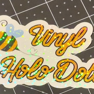 Puede incluir: Una pegatina hologr&aacute;fica con las palabras "Vinyl Holo Dots" en escritura naranja. Una abeja de dibujos animados con rayas negras y amarillas y alas azules est&aacute; a la izquierda. La pegatina tiene un borde blanco y un efecto brillante.