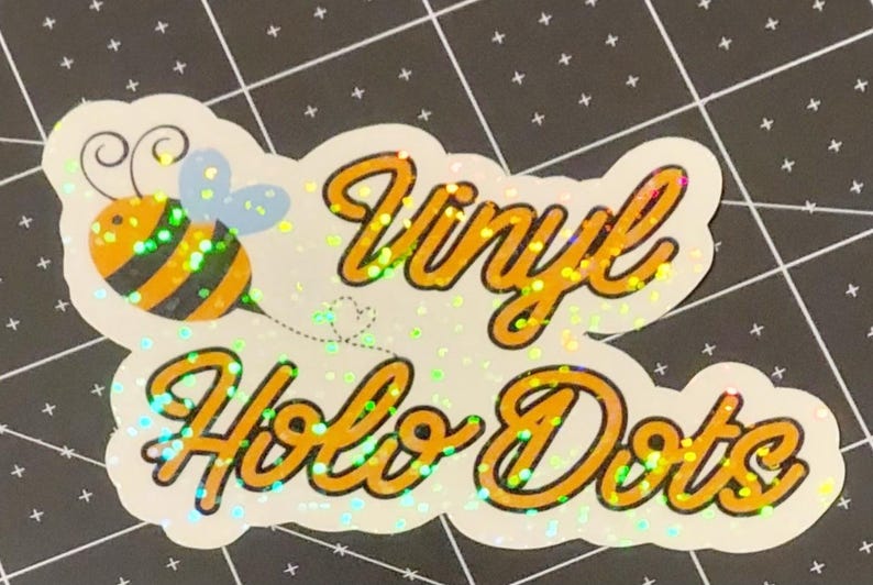 Puede incluir: Una pegatina hologr&aacute;fica con las palabras "Vinyl Holo Dots" en escritura naranja. Una abeja de dibujos animados con rayas negras y amarillas y alas azules est&aacute; a la izquierda. La pegatina tiene un borde blanco y un efecto brillante.