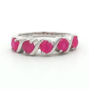 Puede incluir: Un anillo de plata de ley con cinco piedras redondas de color rojo rosado vibrante, engastadas en una banda de metal continua y fluida. El interior del anillo tiene grabado claramente el sello 925 QJ, que indica la composición de plata de la pieza.