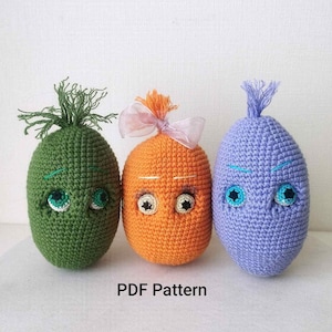 May include: Three handmade crochet dolls in green, orange, and purple. Each doll has a unique face with embroidered eyes and a tuft of yarn or a bow on top. The text "PDF Pattern" is visible at the bottom.
