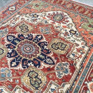May include: A detailed, close-up view of a red, blue, and cream-colored oriental rug. The rug features a central medallion design with intricate floral and geometric patterns. The border is a mix of blue, orange, and cream, adding to the rug's overall ornate appearance.