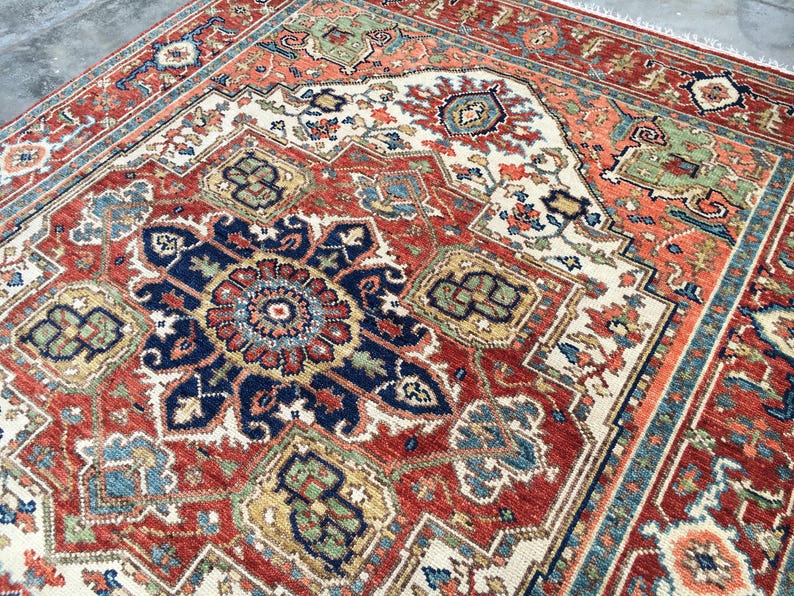 May include: A detailed, close-up view of a red, blue, and cream-colored oriental rug. The rug features a central medallion design with intricate floral and geometric patterns. The border is a mix of blue, orange, and cream, adding to the rug's overall ornate appearance.