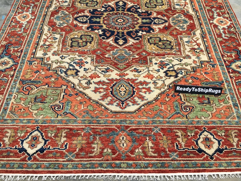 May include: A rectangular rug with a detailed, symmetrical design. The rug features a central medallion in navy blue and rust-red, surrounded by cream, green, and gold patterns. The border is a deep red with intricate motifs, and the text "ReadyToShipRugs" is visible.