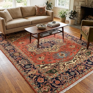 Peut inclure: Un grand tapis rectangulaire orné d'un médaillon central et de motifs floraux complexes dans des tons terre cuite, bleu marine, crème et vert sauge, terminé par des franges blanches sur les bords courts sur un parquet.