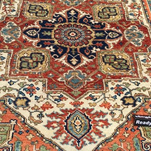 May include: A detailed close-up of a Persian-style rug with a central medallion design. The rug features a complex pattern in shades of red, navy, cream, and green. The intricate design includes floral and geometric elements, creating a rich, textured appearance.